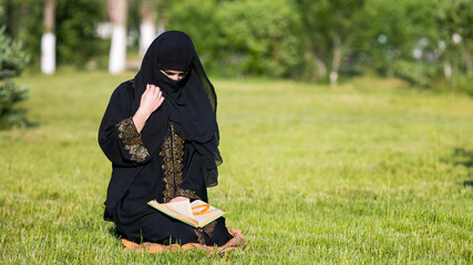 Islamic woman prayer in a city park. Islamic woman performs morning prayer sitting on green grass in park.