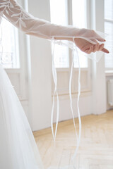 Beautiful slender blonde in the evening sun in a long white dress near a large window. Perfect hair and makeup for the bride, a new collection of wedding dresses