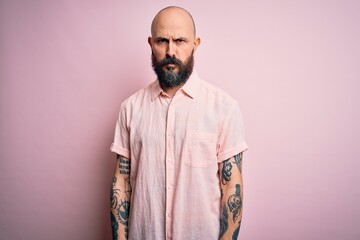 Handsome bald man with beard and tattoo wearing casual shirt over isolated pink background skeptic and nervous, frowning upset because of problem. Negative person.