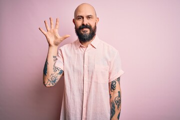 Handsome bald man with beard and tattoo wearing casual shirt over isolated pink background showing and pointing up with fingers number five while smiling confident and happy.