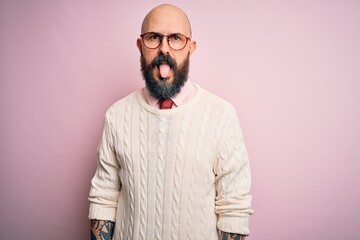 Handsome bald man with beard and tattoo wearing glasses and sweater over pink background sticking tongue out happy with funny expression. Emotion concept.