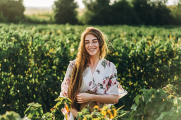 beautiful woman with long curly hair and freckles face on currant field background. Girl in a light dress walks in the summer sunny day