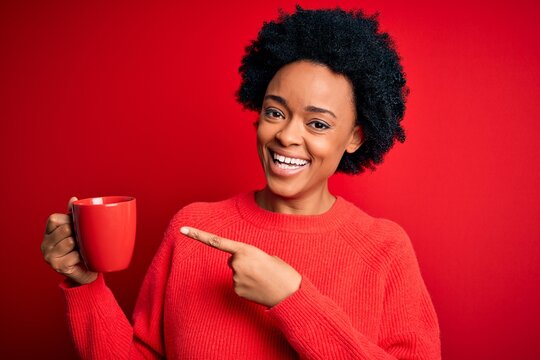 African American afro woman with curly hair drinking cup of coffee over red background very happy pointing with hand and finger