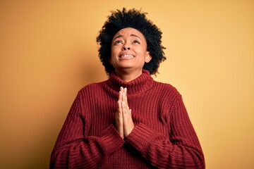 Young beautiful African American afro woman with curly hair wearing casual turtleneck sweater begging and praying with hands together with hope expression on face very emotional and worried. Begging.