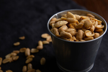 A pile of peanuts in a zinc cup on a black top