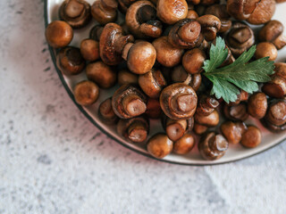 Ready-to-eat fried mini champignons on plate with copy space. Perfect mini mushrooms heap on plate over gray cement background. Top view or flat lay.