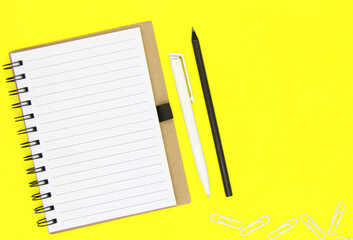 Back to school. Educational concept, office supplies. Craft Notebook, black pencil and white pen on an isolated yellow background. Copy space. Flatly. The view from the top.