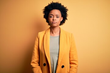 Fototapeta na wymiar Young beautiful African American afro businesswoman with curly hair wearing yellow jacket Relaxed with serious expression on face. Simple and natural looking at the camera.