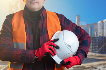 Man works at a construction site. Man in form of a builder. Worker holds a white helmet. Concept -...