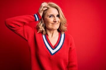 Middle age beautiful blonde woman wearing casual sweater over isolated red background confuse and...