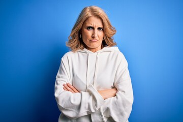 Middle age beautiful blonde sportswoman wearing sportswear over isolated blue background skeptic...