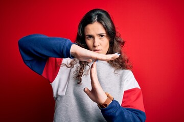 Young beautiful woman with curly hair wearing casual sweatshirt over isolated red background Doing...
