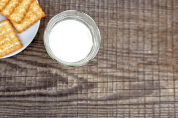 Glass with milk and a white plate with cracker on an old wooden background.