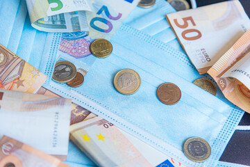 Medical face mask and money on a black background. World coronavirus epidemic and economic losses concept. Concept of financial impact of covid-19 on European money area.