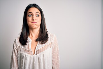 Fototapeta premium Young brunette woman with blue eyes wearing casual t-shirt over isolated white background puffing cheeks with funny face. Mouth inflated with air, crazy expression.
