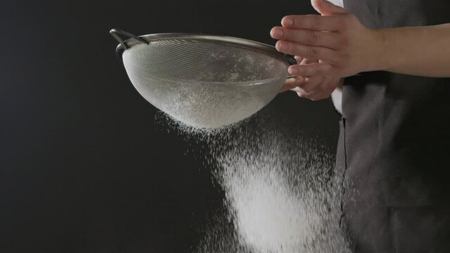 Woman sieves flour through the sifter on a black background. Slow motion, Full HD video, 240fps, 1080p. Process preparing of homemade pastry.