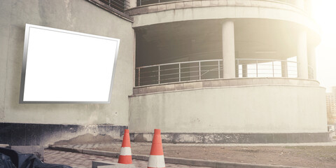 blank billboard on grey wall of multistorey parking and road cones on paved sidewalk