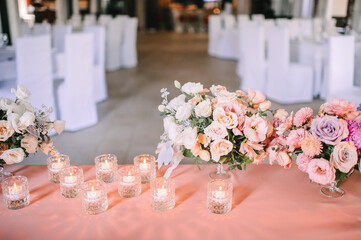 Presidium, banquet table with a pink tablecloth. Plates and cutlery, purple glasses, napkins, candles in glass candlesticks. Bouquet of flowers, asters, roses, carnations, eustomas.