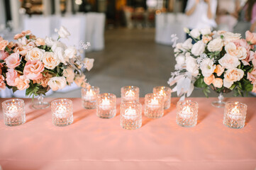 Presidium, banquet table with a pink tablecloth. Plates and cutlery, purple glasses, napkins, candles in glass candlesticks. Bouquet of flowers, asters, roses, carnations, eustomas.