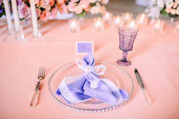 Presidium, banquet table with a pink tablecloth. Plates and cutlery, purple glasses, napkins, candles in glass candlesticks. Bouquet of flowers, asters, roses, carnations, eustomas.