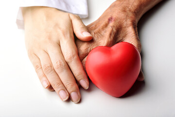 Elderly care concept, Young doctor holding senior patient hand to help and support with red heart,...