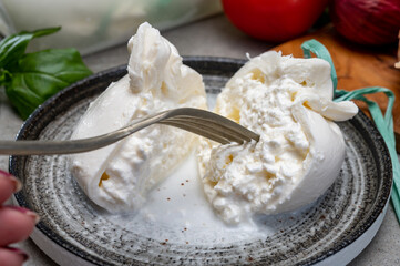 Eating of fresh handmade soft Italian cheese from Puglia, white balls of burrata or burratina cheese made from mozzarella and cream filling