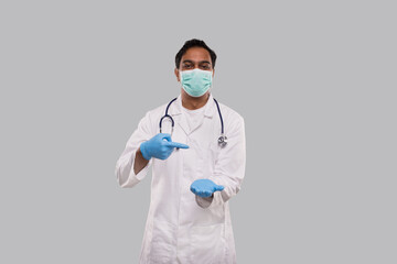 Doctor Pointing at Empty Open Hand in front of Chest Wearing Medical Mask and Gloves Isolated. Indian Man Doctor Advertisment Concept