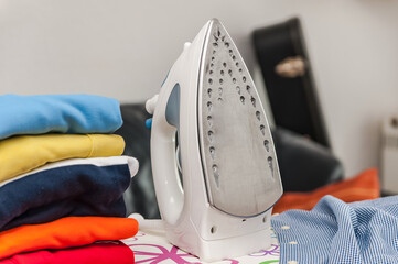 Electric iron and pile of clothes on blurred background