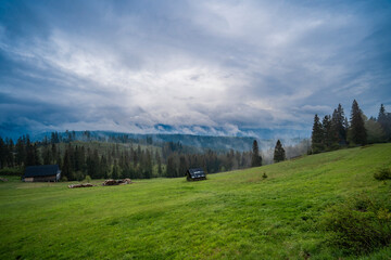 Fototapeta na wymiar Panorama of mountains in the clouds. Meadow and a house