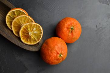 Dry orange slices in wooden plate and fresh oranges on dark slate background