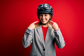 Young beautiful blonde motorcyclist woman wearing motorcycle helmet over red background smiling cheerful showing and pointing with fingers teeth and mouth. Dental health concept.