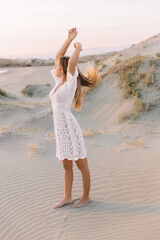 Fototapeta na wymiar Portrait of happy young woman in white dress, on the sand dunes next to the sea. in summer time, on the sunset.