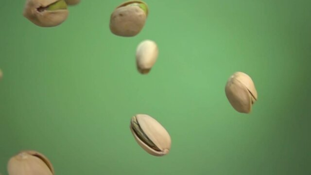 Close up of salted pistachios flying diagonally and spinning on green background in slow motion