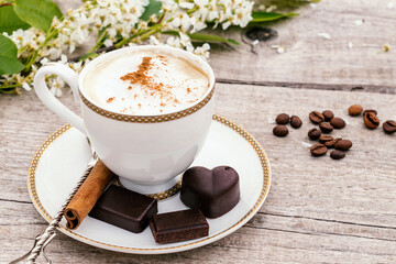 Сup of coffee and homemade chocolate sweets on a wooden background.Coffee beans, white flowers and cinnamon sticks adorn the composition.Сoncept of healthy food and healthy desserts.