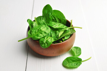 Spinach leaves in wooden bowl over white wooden table background. Vegan food trend. Green living concept.