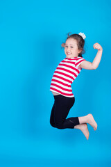 A playful energetic little girl jumps in the air, an copy space in the Studio is filmed isolated on a colorful blue background