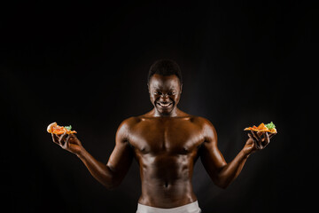 Black handsome naked man with a pizza. Safety food delivery for people who stays at home. Sexy african man shows 2 pieces of pizza in his hands. Tasty food from pizzeria restaurant
