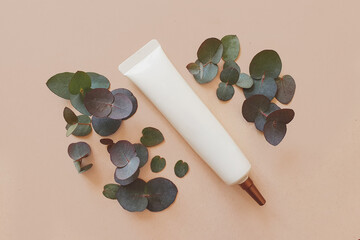 Top view of face and eye cream squeeze, cosmetic tube with long nozzle and bronze screw cap. Mock-up. Craft background with green eucalyptus. space for a text