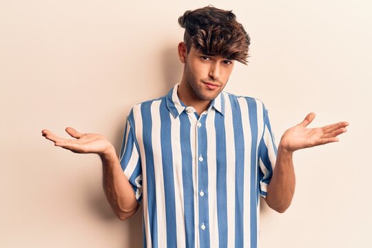 Young hispanic man wearing casual clothes clueless and confused with open arms, no idea and doubtful face.