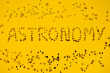 Astronomy word written with small golden glitter stars on a bright yellow background.