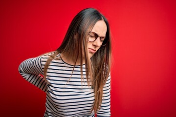 Young beautiful blonde woman with blue eyes wearing glasses standing over red background Suffering of backache, touching back with hand, muscular pain