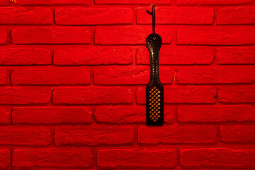 top view of black spanking paddle on red brick wall