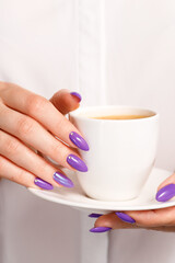 Girl in a white shirt with a beautiful lilac manicure holds a cup of coffee, coffee break concept