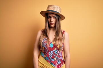 Young beautiful blonde woman wearing swimsuit and summer hat over yellow background skeptic and...