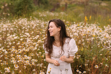 Young beautiful girl in white dress laughing in chamomile field