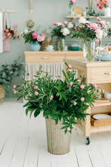 Peony flowers bouquet at the wooden kitchen island on the bright wooden handmade kitchen. Flowers in tall golden tin bucket.