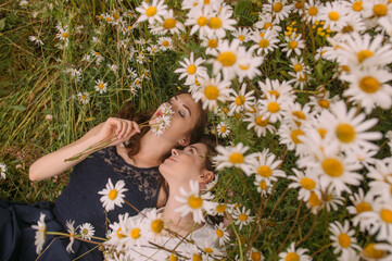 Obraz na płótnie Canvas Two girls in dark blue and white dresses in sunny day lying down and smelling chamomile