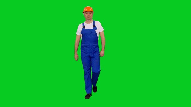 Asian worker in blue coveralls and hard hat walking slowly on green screen background, Chroma key 