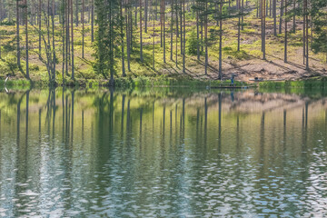 sky and tree reflection in secluded area by the lake. Calm waters and cloudy sky. fisherman in the background Sweden. selective focus. long exposure