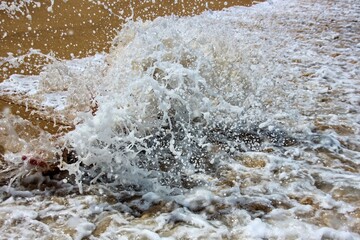 Beautiful white foamy water patterns on shallow sandy ocean beach. Sea water surface with foam and ripples as background. Flowing running sea water on shore of tropical island. Wave splashing close up